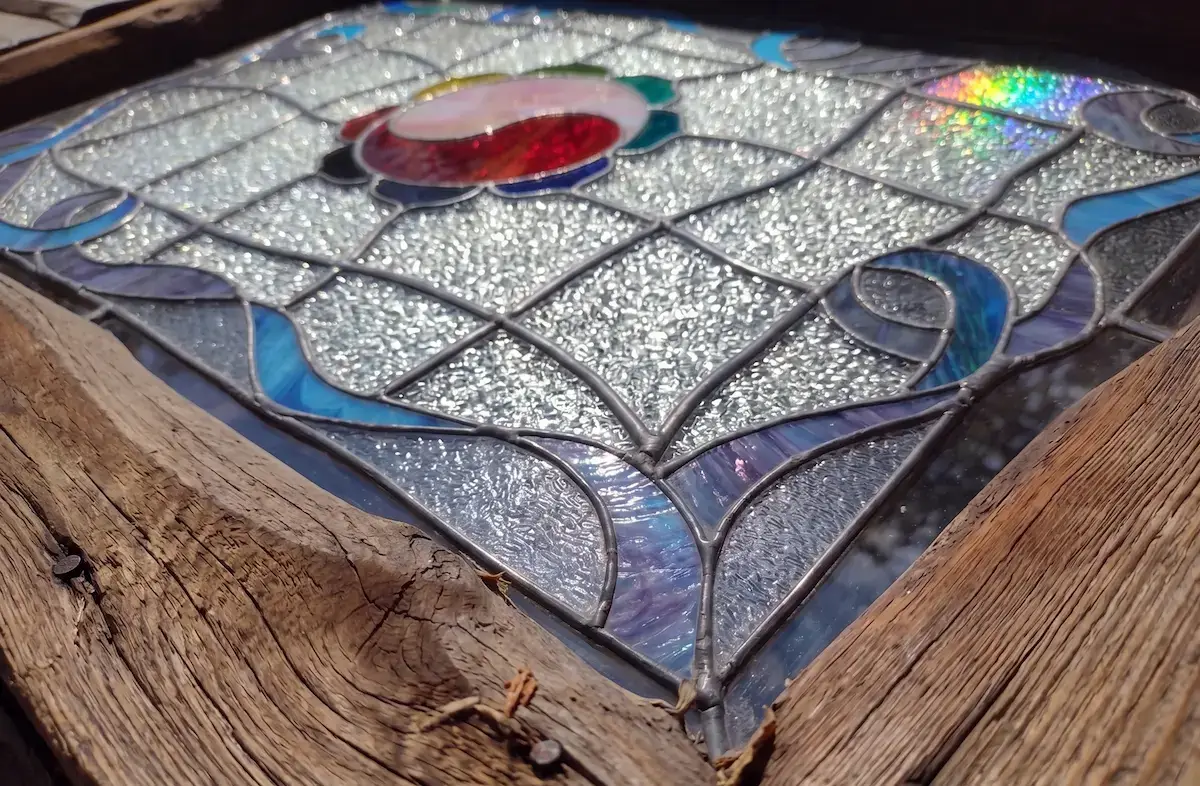 Pieza de vitral con vidrio texturado e iridiscente apoyada sobre madera